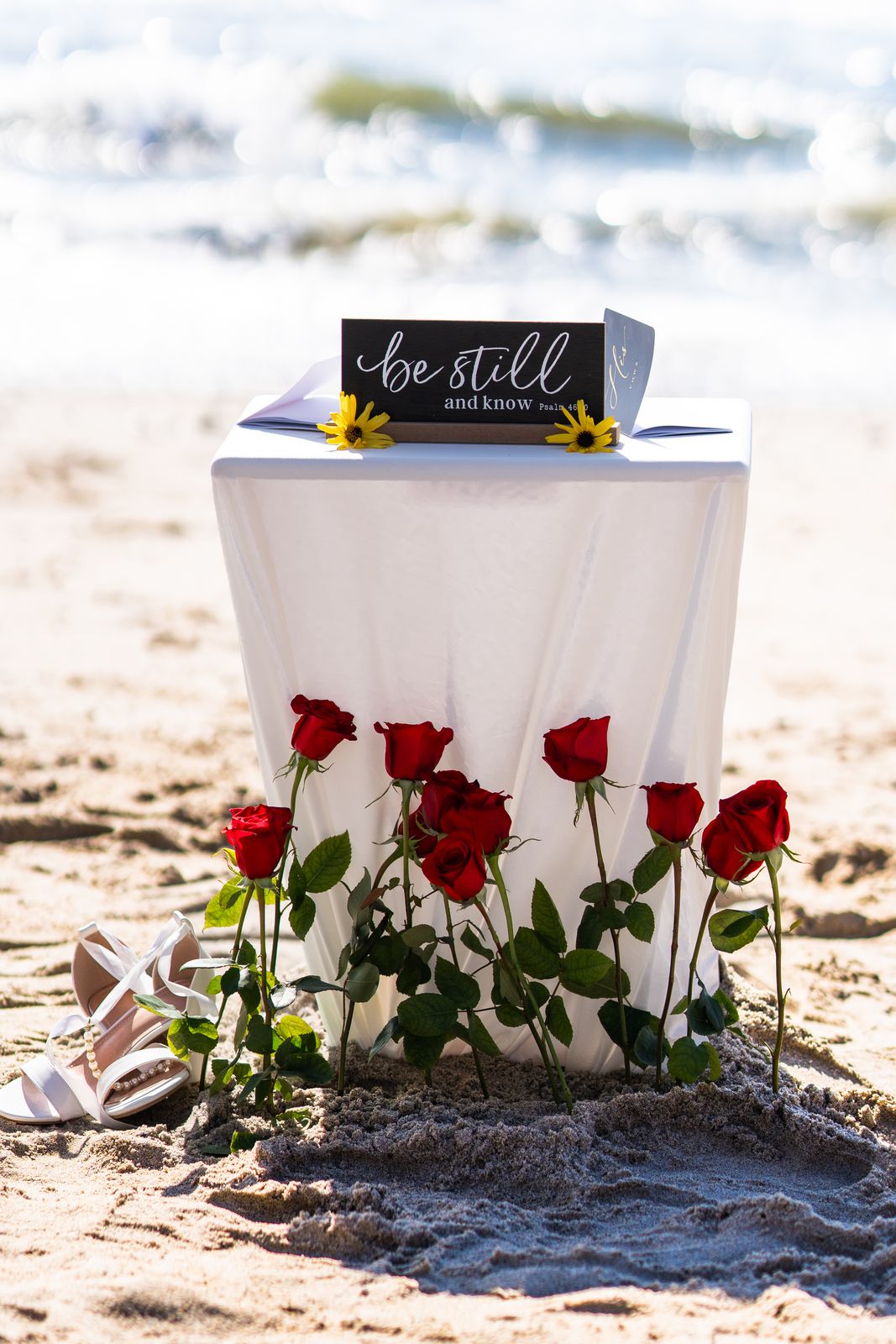 Ceremony table with a be still sign and red roses in the sand
