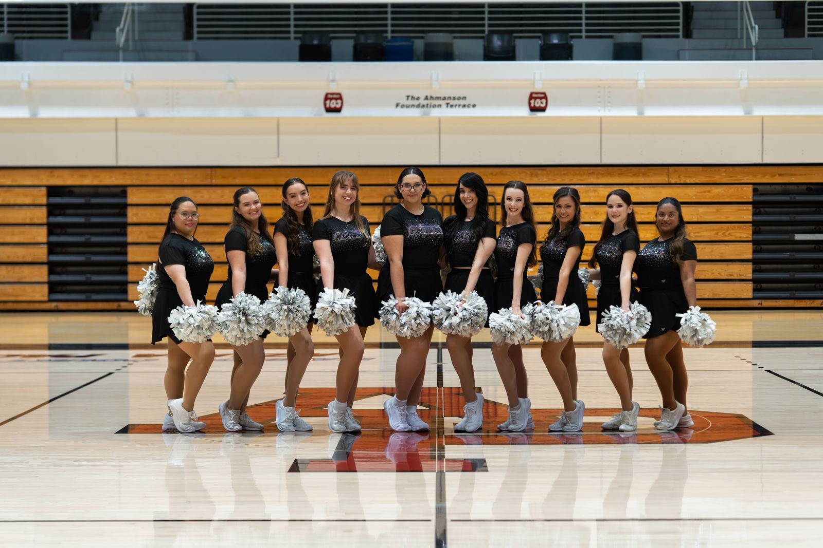 Dance team holding silver pom-poms on a basketball court