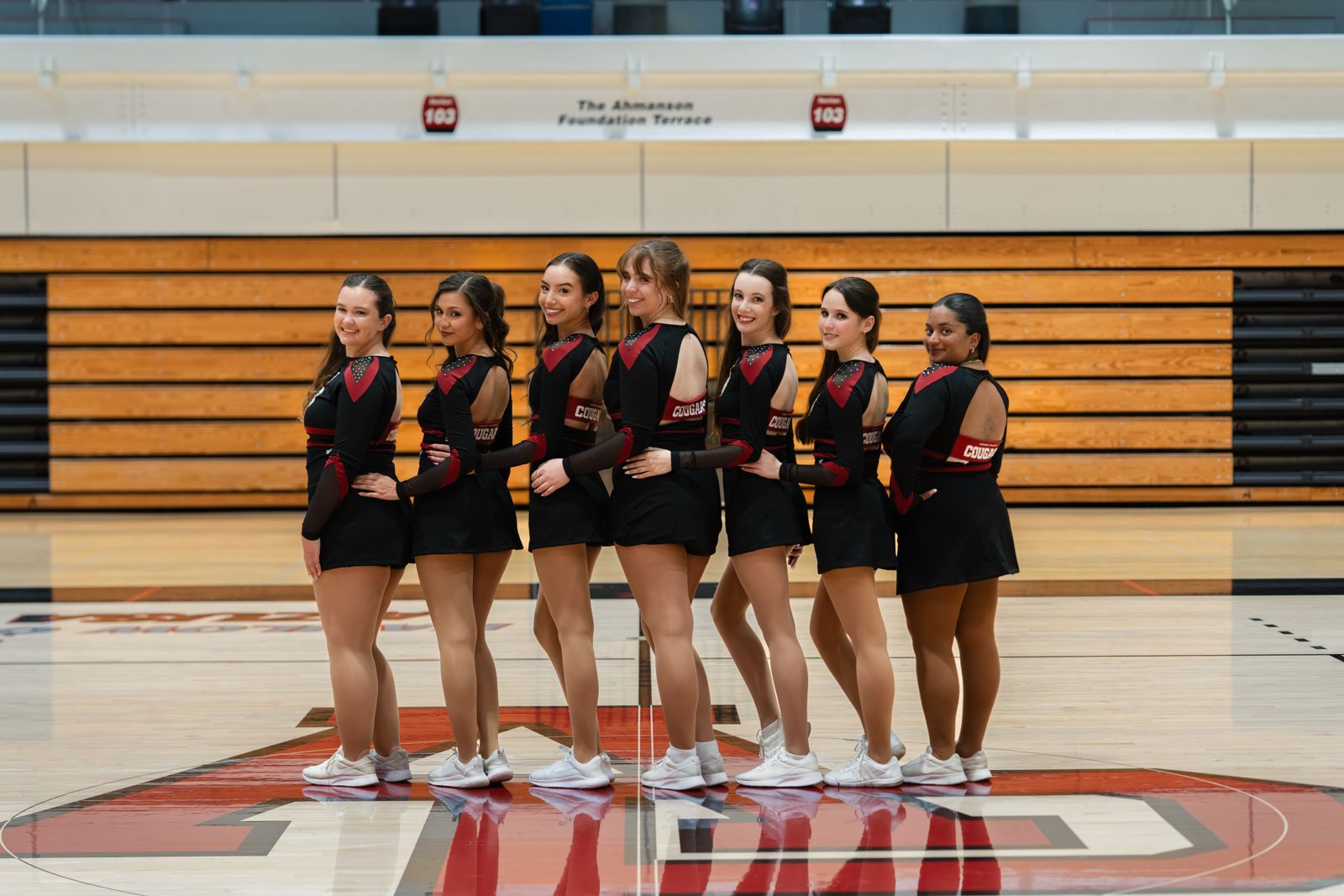 Dance team in black and red uniforms looking back over their shoulders on court