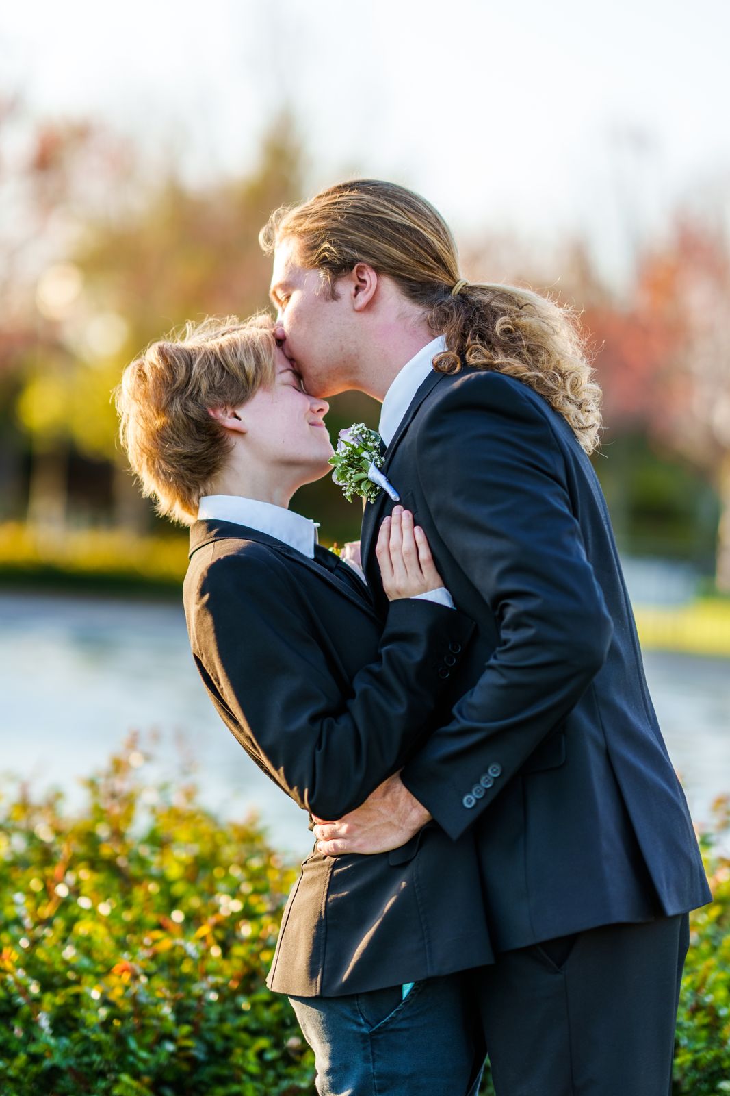 Couple in suits sharing a forehead kiss at sunset