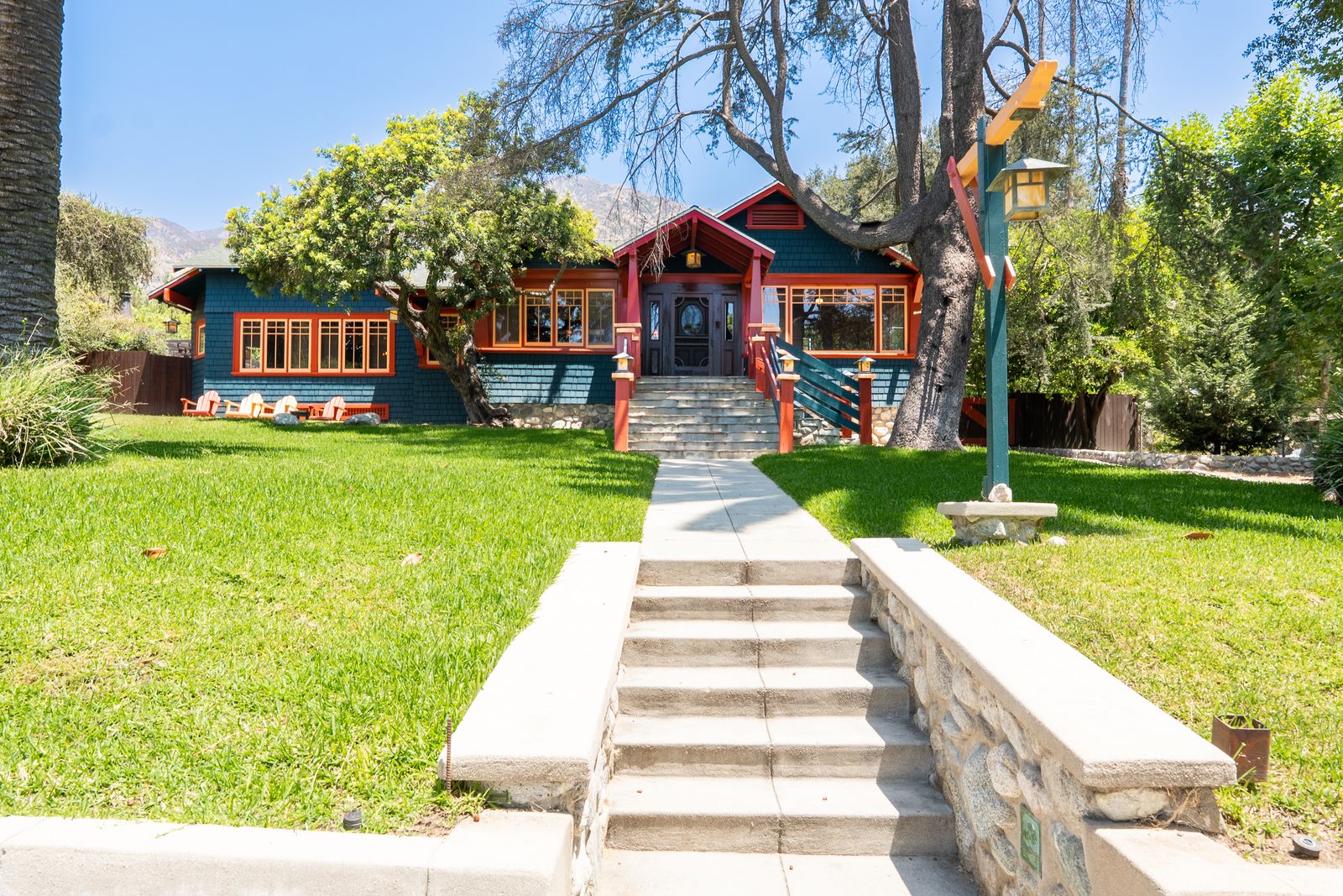 Blue craftsman home with red trim and stone steps up a green lawn